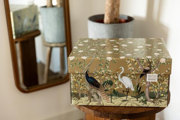 A storage box adorned with the "Golden Paradise" design, showcasing a variety of birds such as a peacock and a white heron amidst lush flora and fauna on a gold background. The box is detailed with illustrations of blooming white flowers, lemon fruits, and dragonflies.